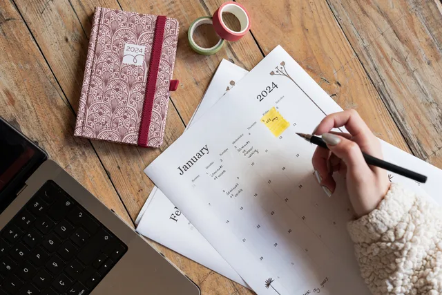 A person plans events in a 2024 calendar beside a notebook and laptop on a wooden desk. Protecting time for decisions that cannot be delegated